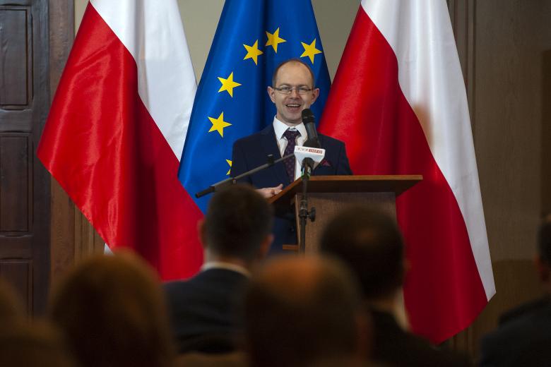 Krzysztof Kurowski przemawia na podium na tle flag Polski i Unii Europejskiej.