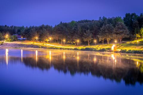 Nocne ujęcie drogi oświetlonej latarniami biegnącej wzdłuż brzegu jeziora