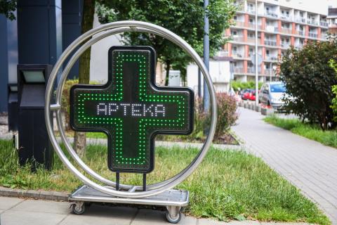 Znak przedstawiający krzyż z napisem "Apteka" w środku stojący na chodniku przy ulicy