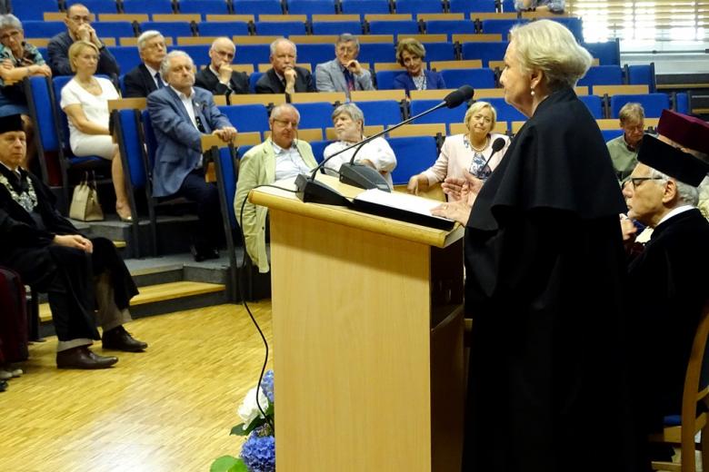 zdjęcie: po prawej kobieta w todze, przed nią na auli wykładowej siedzi kilka osób