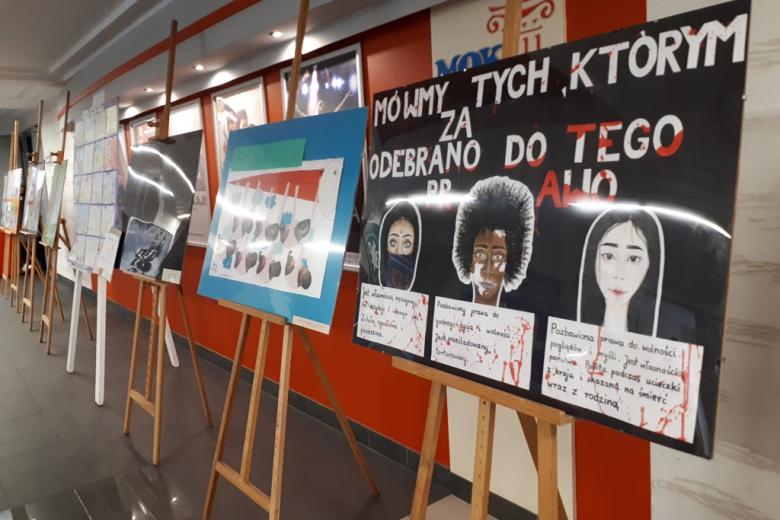 zdjęcie: na korytarzu stoją sztalugi z plakatami wykonanymi przez uczniów
