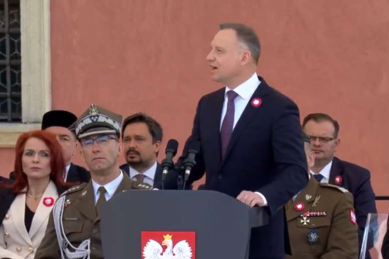 Prezydent RP Andrzej Duda przemawia z podium pod Zamkiem Królewskim w Warszawie. Siedzą za nim uczestnicy uroczystości, w tym RPO Marcin Wiącek.