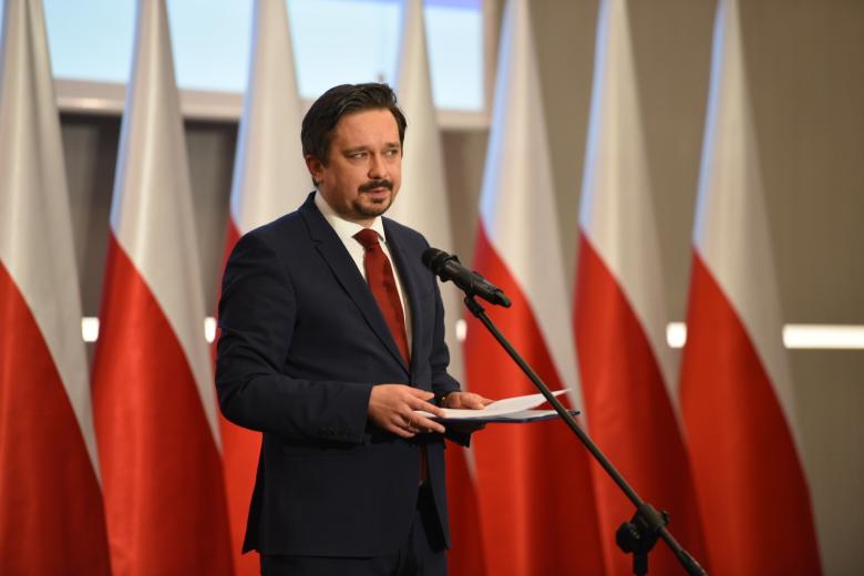 RPO Marcin Wiącek przemawia do stojącego mikrofonu na tle flag Polski