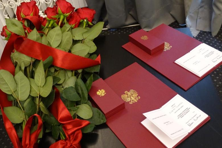 zdjęcie: na stoliku leżą bukiety czerwonych róż i burgundowe teczki z orłem