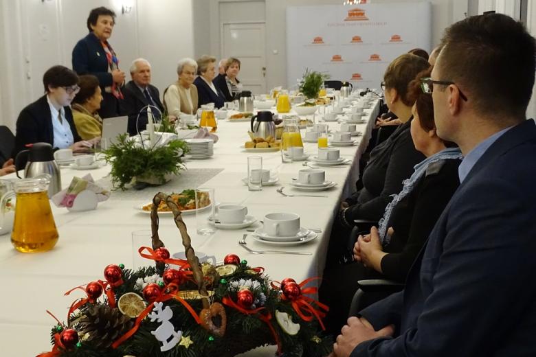 zdjęcie: kilkanaście osób siedzi przy stole, jedna z kobiet stoi