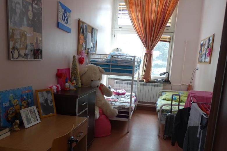 zdjęcie: wnetrze pokoju, w nim łóżko piętrowe stojące pod oknem, biurko, kolorowa firanka