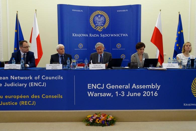 zdjęcie: za granatowym stołem siedzi trzech mężczyzn i dwie kobiety, za nimi widać ściankę z napisem Krajowa Rada Sądownictwa, obok niej stoją polskie i europejskie flagi