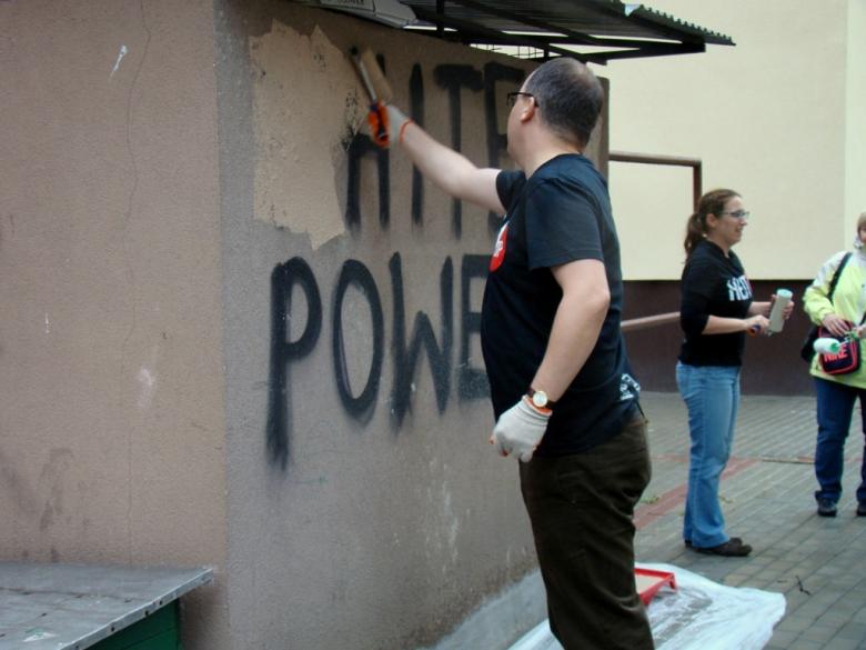 Zdjęcie: mężczyzna w czarnej koszulce zamalowuje napis ma ścianei
