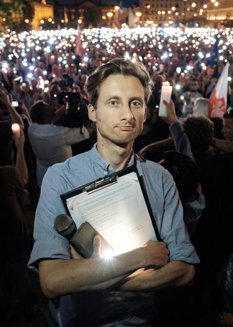 Mężczyzna z podkładką na dokumenty na tle zgromadzonych ludzi ze świecami