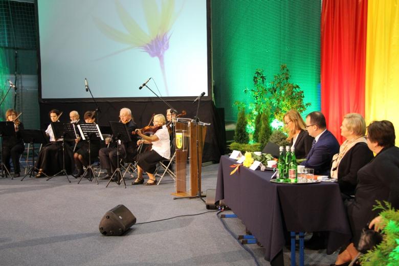 zdjęcie: po lewej stronie widać członków orkiestry, po prawej siedzą cztery osoby za stołem prezydialnym