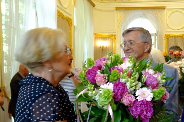 zdjęcie: kobbieta odbiera różowo-kremowe kwiaty od mężczyzny w okularach