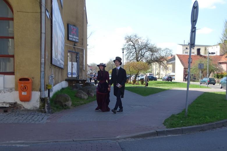 Dwoje młodych ludzi w XIX-wiecznych strojach idzie ulicą