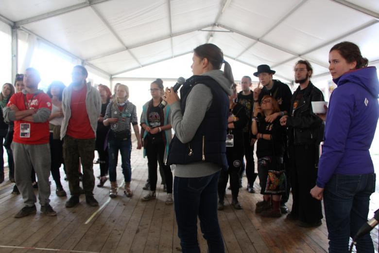 zdjęcie: grupa ludzi stoi w namiocie, na pierwszym planie kobieta mówi coś do mikrofonu