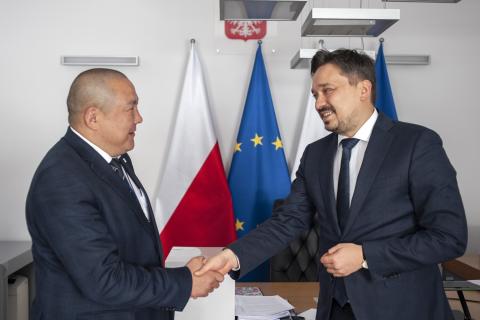 RPO Marcin Wiącek i Ombudsman Mongolii Jargalsaikhan Khunan ściskają dłonie na tle flag Polski i UE