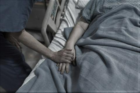 ręka meżczyzny dotyka dłoni kobiety leżącej na szpitalnym łóżku 