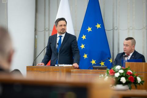 RPO Marcin Wiącek wypowiada się z mównicy w sali plenarnej Senatu. W tle flagi Polski i Unii Europejskiej