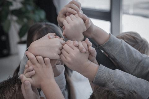 Grupa dzieci trzymających się za uniesione ponad głowami dłonie
