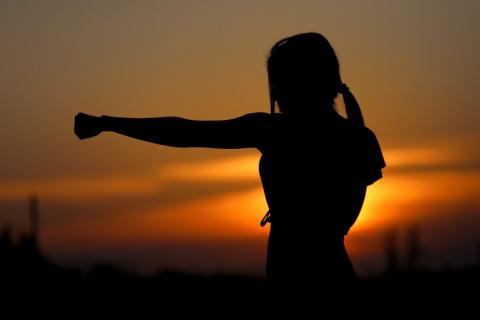 Kobieta z wyciągniętą ręką o zaciśniętej pięści (ruch karate) na tle zachodzącego słońca